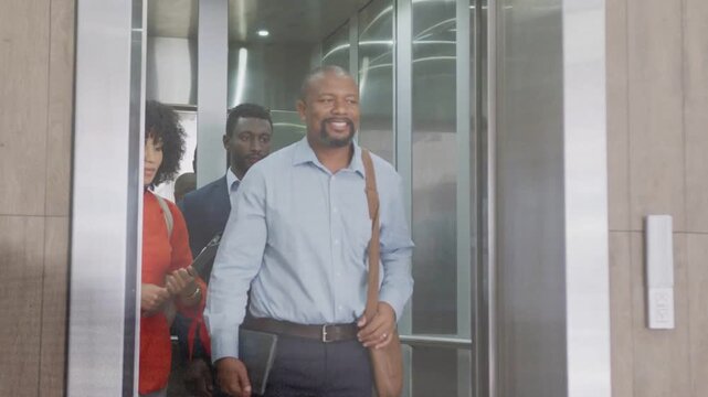 Lead man stepping through elevator doors opening, team following, tablet showing business agenda