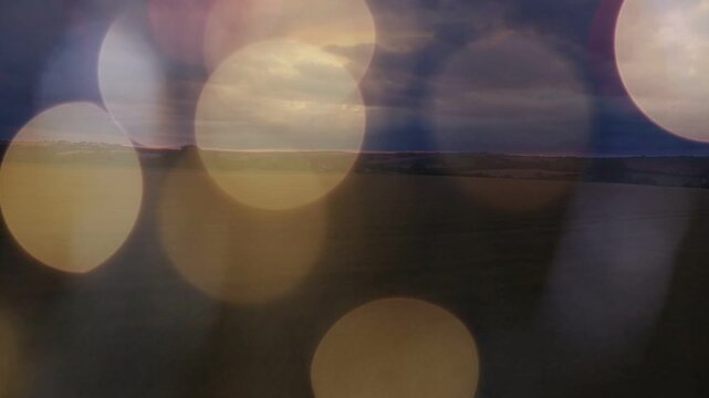 Dusk light shifting, bokeh circles drifting and fading, revealing thin horizon band and clouds