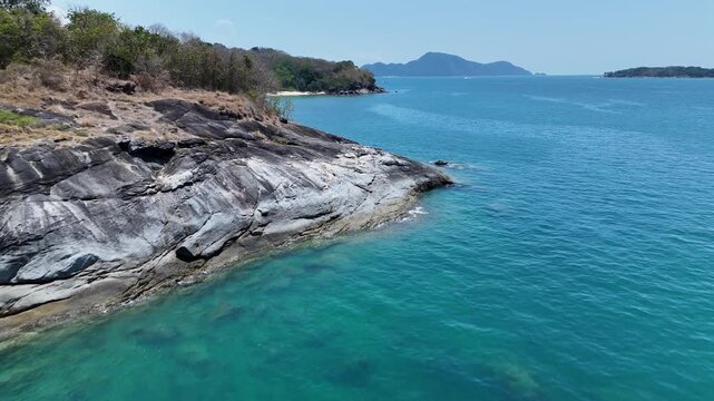 Serene Rocky Coastline with Clear Turquoise Water and Distant Islands Under Bright Blue Sky in Natures Beauty