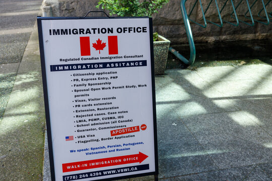 A VSWI Immigration Office sandwich board listing Canadian visa, work permit, citizenship and apostille services on a downtown Vancouver sidewalk.