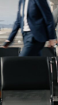 Vertical video Travelers walking in busy airport departure terminal, standing up from chairs to go to boarding gate. Young girl, senior man and other people flying home during holiday rush