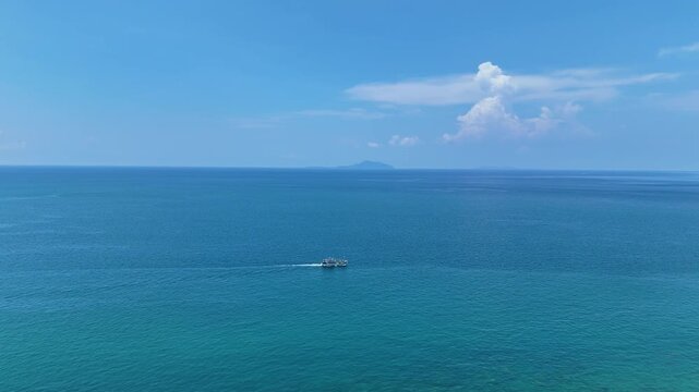 Small Boat Sails Across Vast, Calm Blue Sea Under Clear Sky with Distant Clouds and Island on Horizon, Evoking Tranquility and Freedom