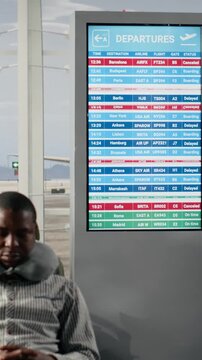 Vertical video Angry passengers in airport seeing red on departure board screen caused by flight delays, shouting and making phone calls. Frustrated traveler upset by flight cancelation on FIDS