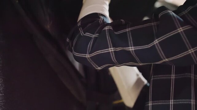 Trainer adjusts rider saddle straps. Equestrian trainer securing stirrup straps during saddle adjustment. Stable environment where trainer carefully fits and secures horseback riding equipment
