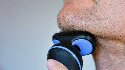 A close-up shot of a man grooming his facial stubble with a modern electric razor. © Stepan Popov