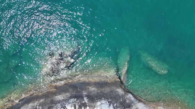 Aerial View of Rocky Coastline with Clear Turquoise Water and Sunlight Reflecting Surface, Capturing Stunning Aerial View of Rocky Coastline with