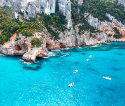 Aerial view of rocks and mountains, blue bay, beach, boats on sunny summer day. Cala Goloritze, Sardinia Island, Italy. Top drone view of cliffs, stones, green trees, turquoise water. Tropical. Ocean