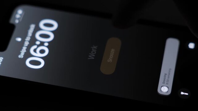A smartphone screen lights up in the dark as a 6 AM alarm turns on with the label Work, showing an early morning wake-up moment on a mobile device in low light. High quality 4k footage