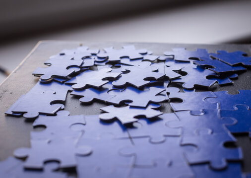 Hand placing last orange puzzle piece in blue jigsaw, completion concept, close up. Hand, puzzle piece, orange, blue, placing, last, completion, close up