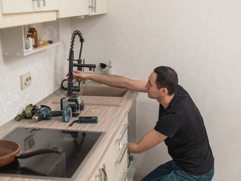 A plumber is replacing a faucet in the kitchen.