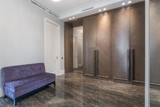A modern room with a polished stone floor. A purple couch sits against one wall while a large closet takes up another side. The lighting is bright and inviting