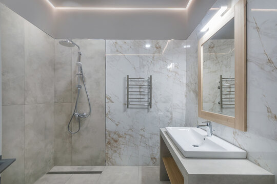 A stylish bathroom features marble walls and a shower with a sleek design. A mirror sits above the sink, reflecting the light from the ceiling