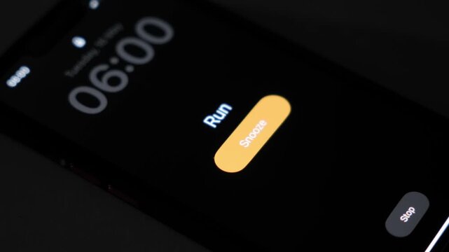 A smartphone alarm rings at 6 AM with the run label on a dark screen showing a snooze button and an early morning wake up moment before a workout. High quality 4k footage