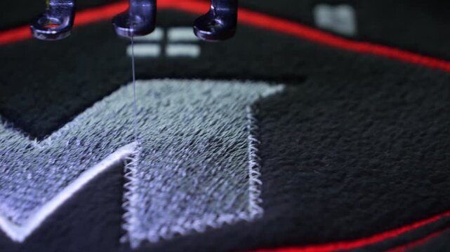 Machine embroidery on a black fleece blouse with red and grey thread. House roof embroidery. Selective focus close-up.