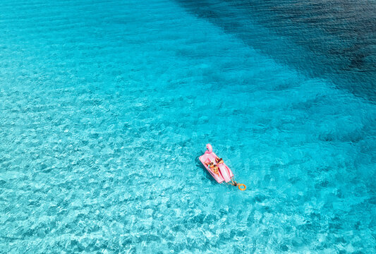 Aerial view of Inflatable pink flamingo with people on crystal clear blue water on summer sunny day. Top drone view of relax family on boat, turquoise sea in Sardinia Island, Italy. Summer holidays