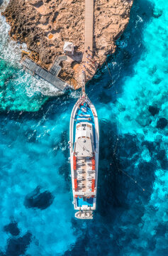 Aerial view of boat with people and rocky sea coast on sunny summer day. Top drone view of yacht, transparent azure water, path. Mediterranean sea. Travel in Sardinia island, Italy. Tropical landscape