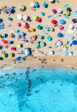 Aerial view of colorful umbrellas on sandy beach, swimming people in blue sea on sunny summer day. Sardinia, Italy. Tropical landscape with clear turquoise water. Travel and vacation. Top down view