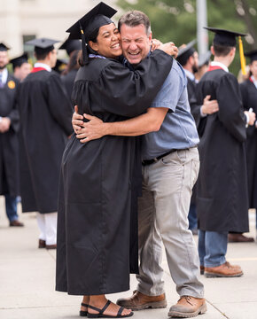 Woman in graduation cap and gown hugging man in celebration outdoors