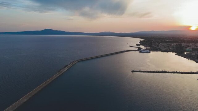 Cinematic Aerial View of Long Harbor Breakwater at Sunset, Golden Light Over Calm Mediterranean Sea and Coastal City of Kalamata in Greece