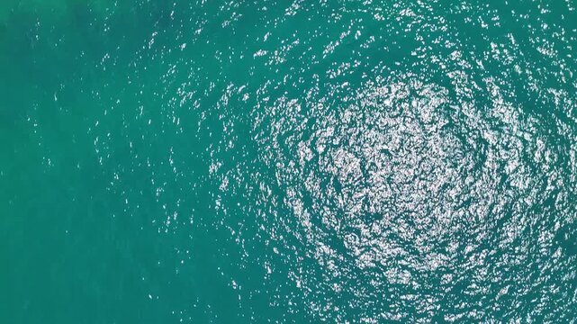 Aerial View of Shimmering Turquoise Sea with Sunlight Reflection Water Surface Creating Mesmerizing Pattern and Rocky Coastline Showcasing Natural