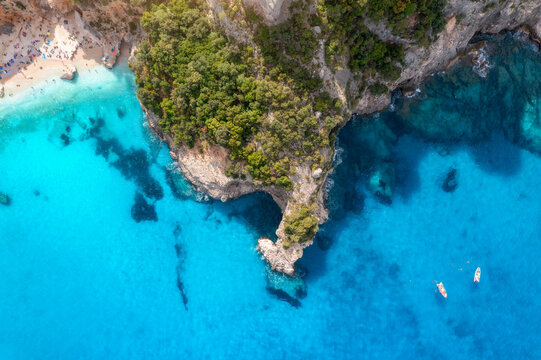 Top down view of boats in turquoise water on summer sunny day. Aerial drone view of boats in clear blue sea bay, rocks, green forest. Travel in Sardinia, Italy. Tropical seascape. Summer vacation