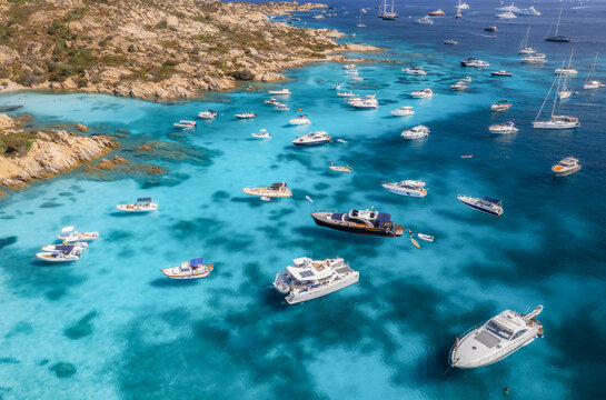 Aerial view of luxury yachts and boats on blue sea, beautiful island, mountain on summer sunny day. Sandy beach, rocky sea coast, azure transparent water in Sardinia, Italy. Top drone view. Seascape