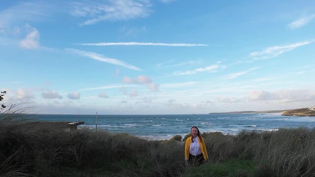 Relaxed Lady Stands On Rocky Coast. Outdoor Enthusiast Smiles Amidst Seaside Landscape And Sky