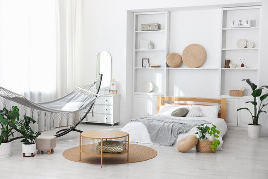 Comfortable hammock, bed and houseplants in room. Interior design
