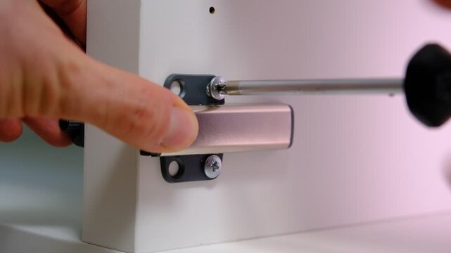 Close-up of screwing a cabinet door buffer latch with a screwdriver