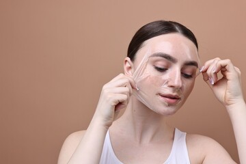 Naklejka premium Beautiful woman peeling off facial mask on brown background. Space for text