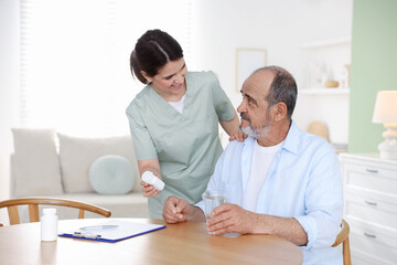 Obraz premium Smiling care worker working with senior man at wooden table at nursing home