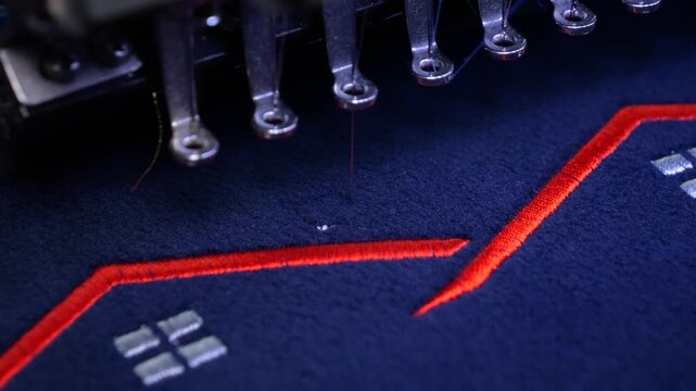 Machine embroidery on a black fleece blouse with red thread. House roof embroidery. Selective focus close-up.