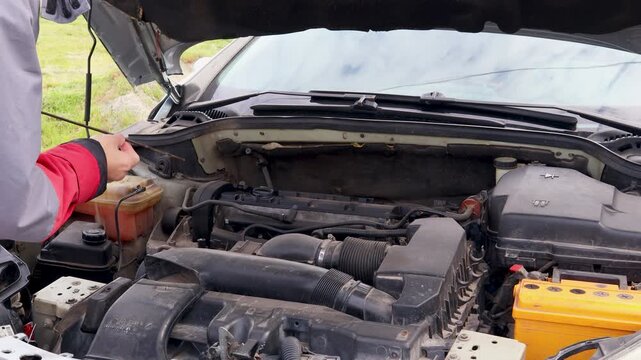 Mechanic opening a car hood and checking the motor engine oil level with a dipstick for maintenance, inspection, and service in an automotive workshop or garage