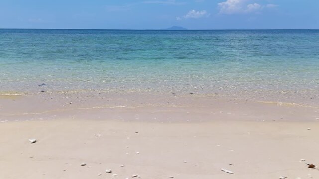 Serene Beach Scene with Clear Blue Water, Sandy Shores, and Distant Island Under Bright Sky with Clouds and Horizon