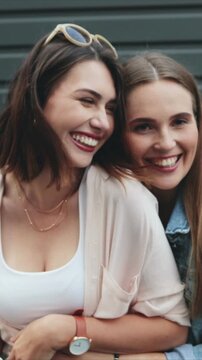 Vertical camera view of two Caucasian women holding instant camera. Female friends laughing while interrupting photo moment. Outdoor setting. Women spending time together while standing close outside.