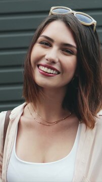 Vertical shot of Caucasian woman holding instant camera in hands. Female smiling at lens with cheerful emotion. Outdoor street setting. Woman preparing to take photo while standing outside in daytime.