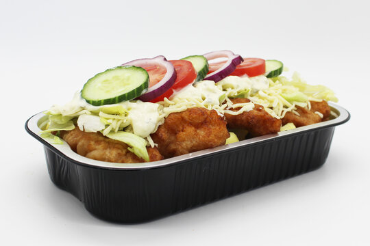 Fried fish kapsalon with fries, salad and garlic sauce in takeaway container, three quarter view on white background