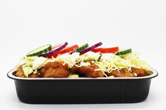 Dutch kapsalon with fried fish, fries, salad and garlic sauce in takeaway container on white background