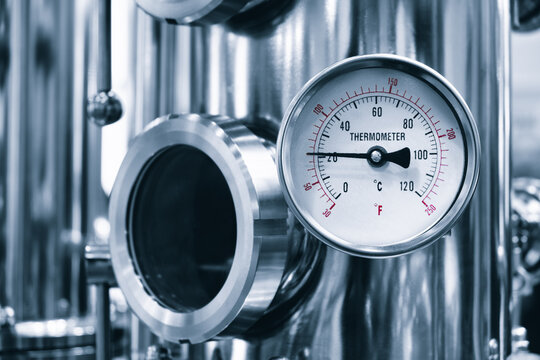 interior of an industrial distillery features tall copper and stainless steel columns. Pressure gauges and pipes indicate the ongoing distillation process. The high ceiling features exposed beams.