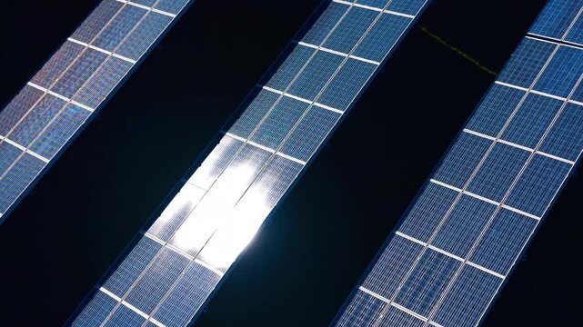 Top view of solar panels with central sun reflection. High angle shot of blue photovoltaic panels with bright sun reflection and dark shadows between rows.
