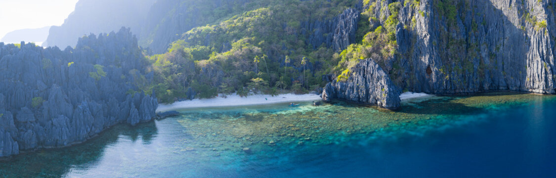 A scenic, secluded beach is surrounded by rugged, karst limestone in El Nido. This area in the Philippines is a popular vacation destination due to its coral reefs, beaches, and hidden lagoons.
