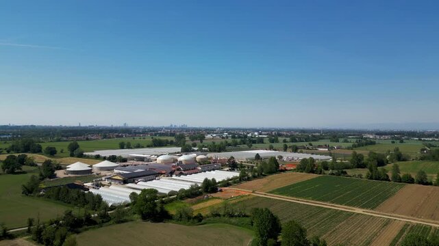 Biogas Plant Facility: An aerial view captures a sprawling biogas plant nestled amongst lush green fields under a clear blue sky, symbolizing renewable energy production and sustainable industry.