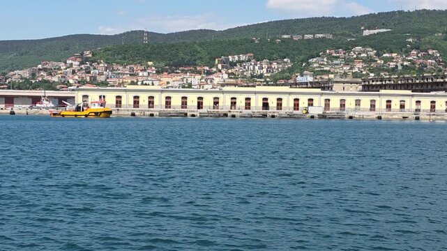 Yellow Workboat Navigating a Coastal Harbor with Hillside Town Background