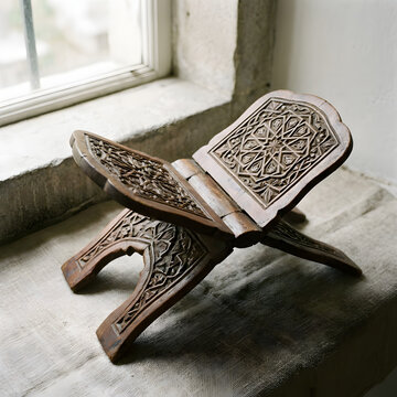 Traditional ornate hand-carved wooden Rehal Quran stand near a window. Elegant Islamic book stand with geometric patterns for Ramadan and Eid decoration. Spiritual heritage and religious woodcraft.
