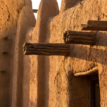 Traditional Sudano-Sahelian mud architecture with protruding wooden toron beams and textured adobe walls in golden hour light. Authentic West African earthen building and cultural heritage site.