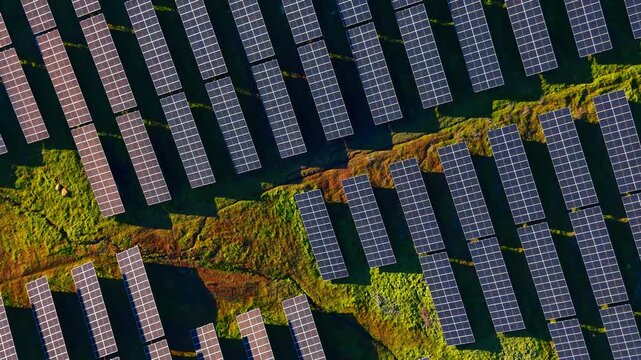 Top down view of solar panels on rocky terrain. Aerial abstract pattern of photovoltaic arrays installed on uneven green and brown ground.