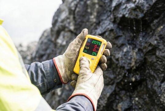 Miner holding portable multi gas detector device near dark rock wall