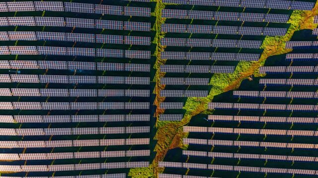 Geometric pattern of solar panels from drone perspective. High angle top down view showing rectangular photovoltaic cells and green vegetation pathways.