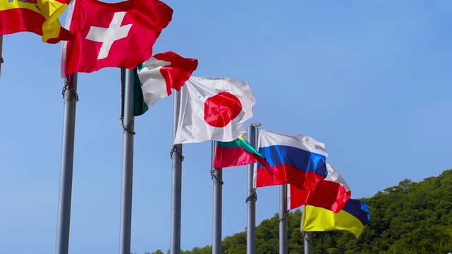 National flags of Switzerland, Italy, Japan, Lithuania, Russia, Poland and Ukraine displayed on tall metal poles under clear blue sky. International cooperation, diplomacy and global relations concept