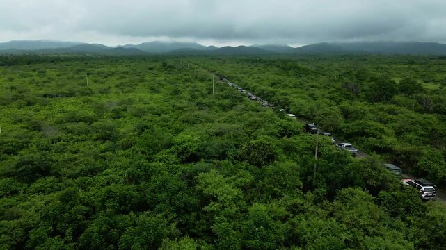 Epic drone push in over off road convoy crossing remote jungle road beneath storm clouds in Ecuador